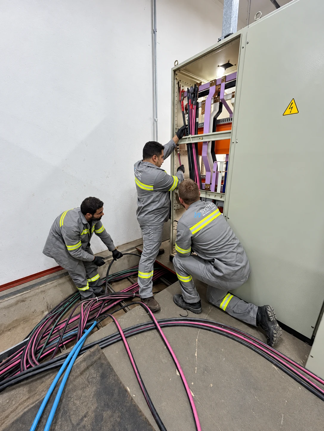 Equipe Systec trabalhando nos barramentos e cabos de um painel de potência.